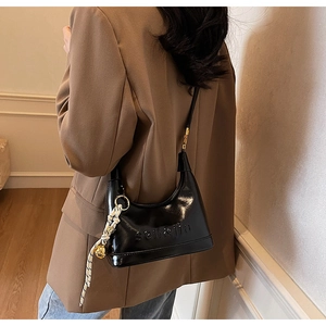 Detail of black patent leather hobo bag with embossed lettering and woven tassel charm
