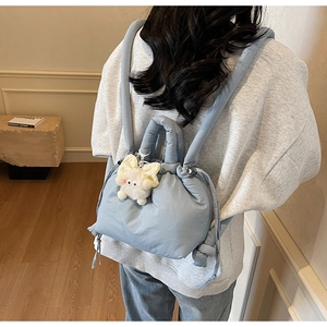 Detail of light blue quilted bucket bag with plush cat charm and padded straps