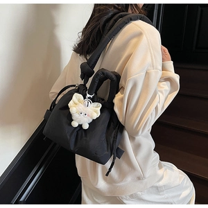 Detail of black quilted bucket backpack with drawstring closure and plush cat pendant