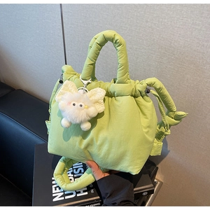 Close-up of light green quilted bucket bag with a cute white plush doll pendant detail