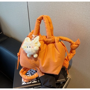 Detail of bright orange quilted bucket bag with knotted rope handle and plush cat charm