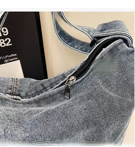 Detailed close-up of smooth metal zipper on blue washed denim tote bag with orange stitching