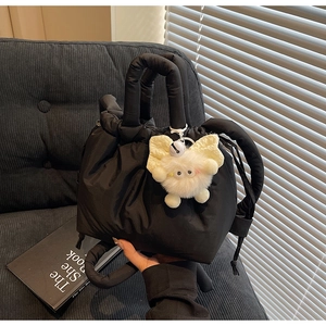 Detail of black quilted bucket bag with drawstring closure and white plush charm