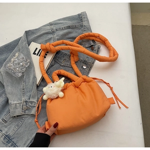 Detail of bright orange quilted bucket bag with drawstring closure and plush bear charm