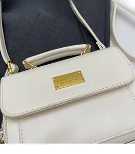 Close-up of white crossbody bag with gold rectangular hardware and textured leather finish