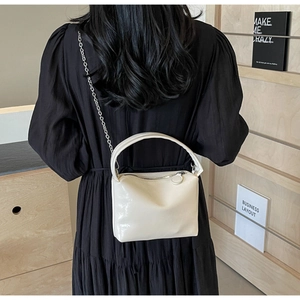 Chic cream patent leather pillow bag with silver chain strap shown on a black dress