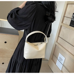Detail of cream white leather pillow bag with chain strap and top handle on model