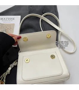 Detail of magnetic snap closures on a white faux leather shoulder bag for easy opening