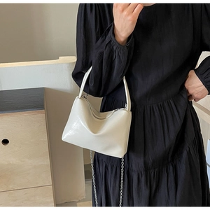 Chic cream pillow bag with silver chain strap worn with a black dress in a modern setting