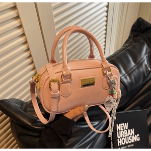 Détail du sac boston en cuir verni rose clair avec plaque et pendentif tressé