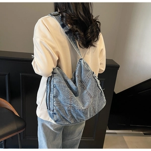 Macro detail of dark blue denim hobo bag featuring frayed edges and contrast stitching