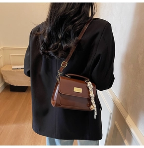 Brown leather crossbody bag with gold hardware and woven pendant detail on black blazer