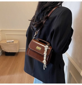 Detail of dark brown crossbody square bag with gold plate and woven rope charm