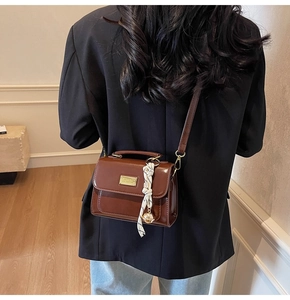 Detail of a brown PU leather crossbody bag with scarf accessory and gold hardware