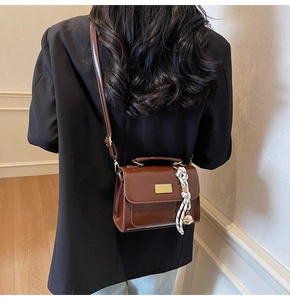 Close-up of brown glossy crossbody bag featuring a striped silk scarf and gold pendant