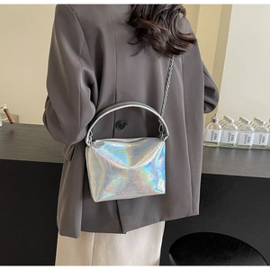 Silver holographic handbag with metal chain strap shown held by a model in a grey blazer