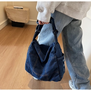 Detail of dark blue denim shoulder bag showing distressed edges and stitching texture