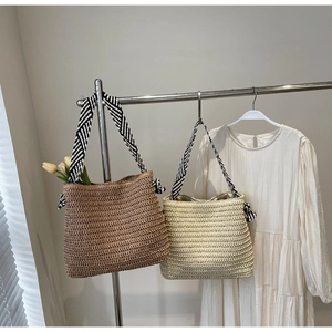 Detail of hand-woven straw tote bags with striped shoulder straps in brown and beige
