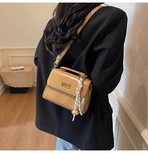 Detail of light brown patent leather crossbody bag with gold plaque and woven charm