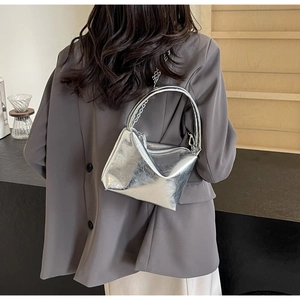 Silver metallic pillow bag shown as a crossbody with chain strap and suit outfit