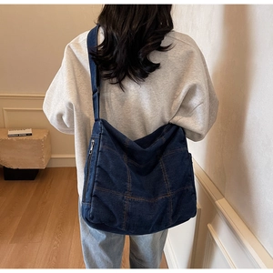 Detail of blue denim tote bag featuring contrast stitching and a side zipper pocket