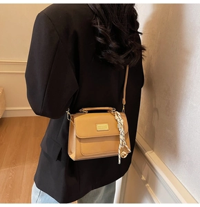 Detail of light brown crossbody bag with metal plaque and checkered scarf accessory