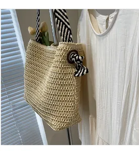 Detail of woven straw tote bag featuring metal grommets and striped cloth handle