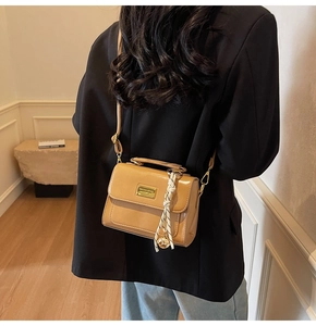 Detail of khaki leather crossbody bag featuring a silk scarf charm and gold plaque
