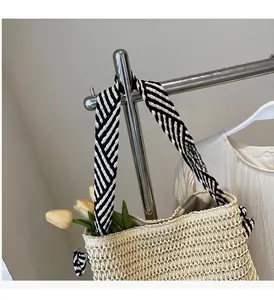 Detail of woven straw tote bag featuring striped black and white handle and mesh texture