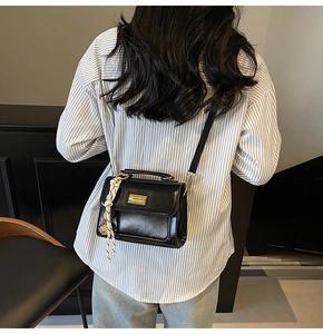 Detail of black minimalist crossbody bag with golden plaque and decorative woven pendant
