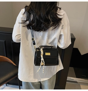 Detail of black glossy leather crossbody bag with gold buckle and striped scarf detail