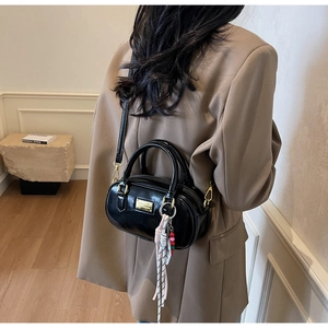 Détail du sac Boston noir brillant avec plaque dorée et accessoire tissé
