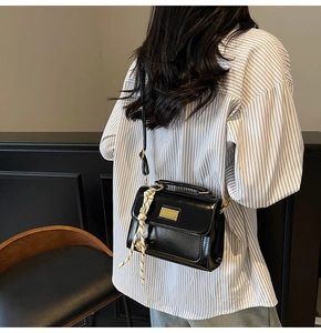 Detail of black glossy PU leather crossbody bag with silk scarf and gold hardware accents