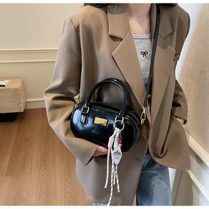 Détail du sac bowling en cuir verni noir brillant avec finitions dorées porté par un mannequin