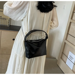 Detail of a shiny black pleated shoulder bag with a silver chain on a model in a dress