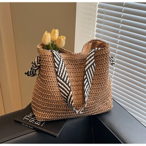 Detail of hand-woven straw tote bag with black and white striped straps and side knot