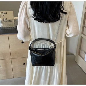 Detail of a black pleated leather mini box bag with a silver chain on a model