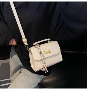 Detail of cream-white crossbody square bag with gold hardware and tassel on model