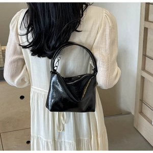 Detail of black glossy leather pillow bag with metal chain handle and silver zipper