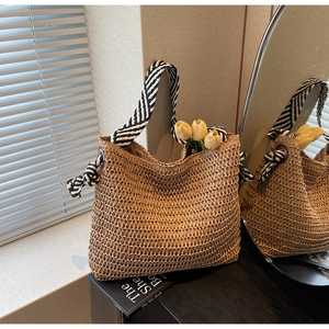 Detail of straw woven tote bag featuring striped shoulder straps and side knot accents