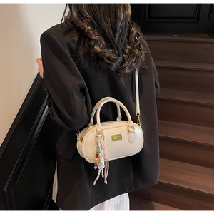 Détail d'un sac bowling beige avec charm tressé sur un mannequin près d'un escalier