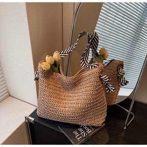 Detail of woven straw tote bag featuring contrast black and white striped shoulder straps