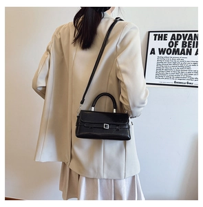 Rear view of a model wearing a black square crossbody bag with top handle and silver hardware