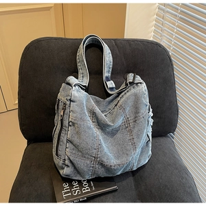Detail of light blue washed denim tote bag featuring side zipper and brown stitching