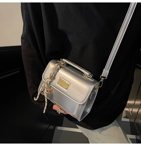 Detail of silver metallic crossbody bag featuring a rectangular plaque and woven charm
