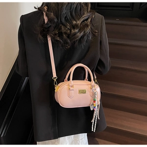 Détail du sac bowling rose en similicuir avec logo doré et pendentif sur un blazer noir