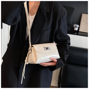 Détail du sac bandoulière crème avec fermoir argenté et nœud tissé sur un blazer noir