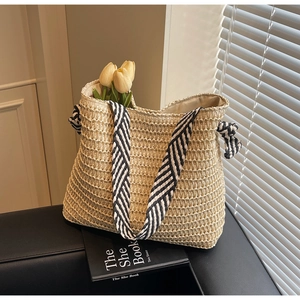 Detail of hand-woven straw tote bag featuring contrast striped handles and texture