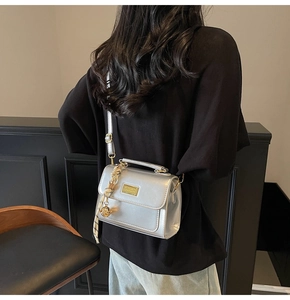 Silver metallic crossbody bag with gold buckle shown on a model in a minimal setting
