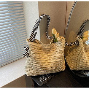 Detail of woven straw tote bag with striped handles and decorative bow in sunlight